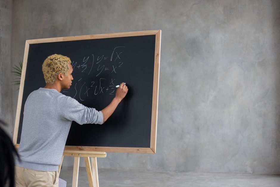 Back view of African American student with marker writing task on blackboard while studying in classroom